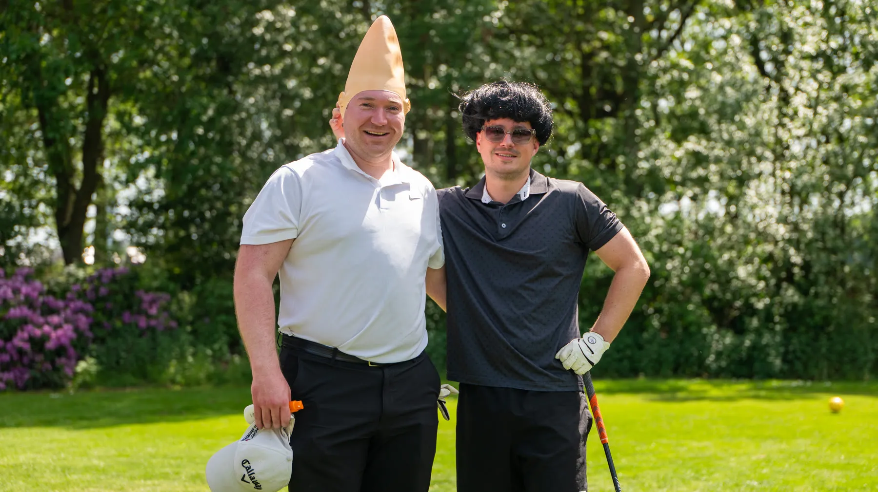 Twee deelnemers, de een met een puntmuts, de ander met een pruik